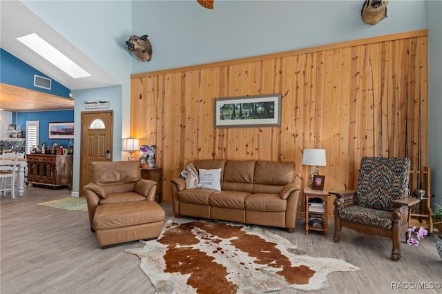 living room with lofted ceiling with skylight, light hardwood / wood-style flooring, and wood walls