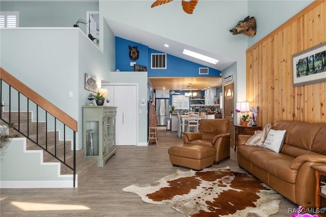 living room with a skylight, hardwood / wood-style floors, high vaulted ceiling, and ceiling fan with notable chandelier