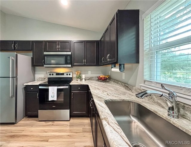 kitchen with light wood-style flooring, a sink, vaulted ceiling, appliances with stainless steel finishes, and light stone countertops