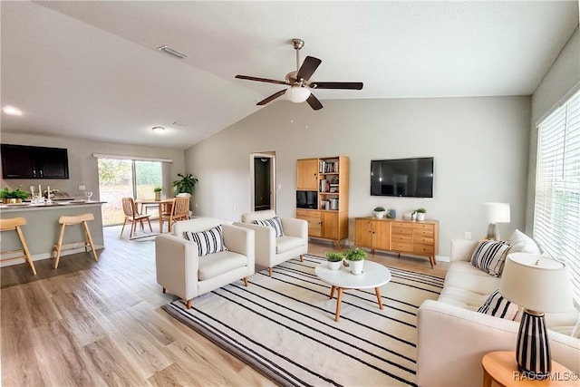 living room with vaulted ceiling, a wealth of natural light, wood finished floors, and visible vents