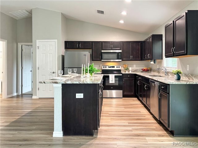 kitchen featuring light stone counters, a center island, stainless steel appliances, lofted ceiling, and a sink