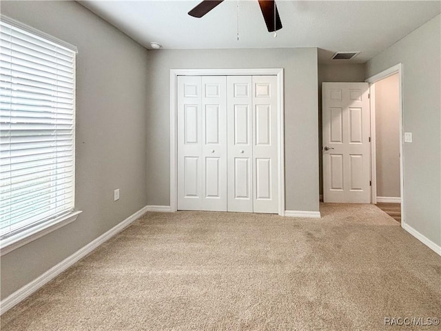 unfurnished bedroom with a closet, light colored carpet, visible vents, ceiling fan, and baseboards