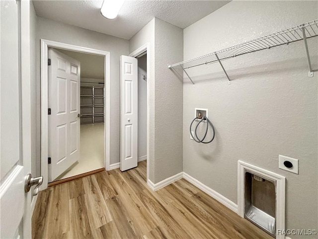 clothes washing area with laundry area, baseboards, hookup for a washing machine, hookup for an electric dryer, and light wood-style floors