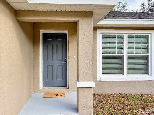 view of exterior entry featuring a shingled roof and stucco siding