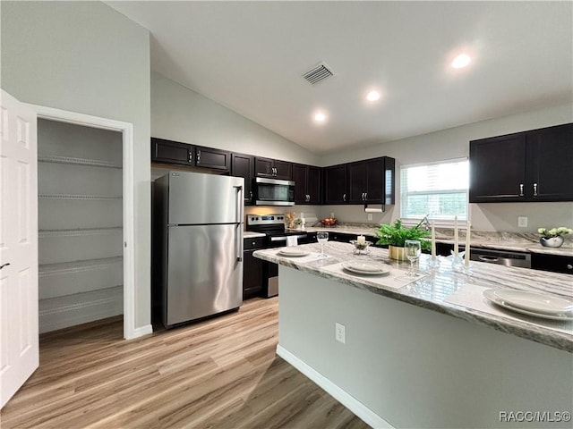 kitchen with dark cabinets, visible vents, appliances with stainless steel finishes, light wood-type flooring, and light stone countertops