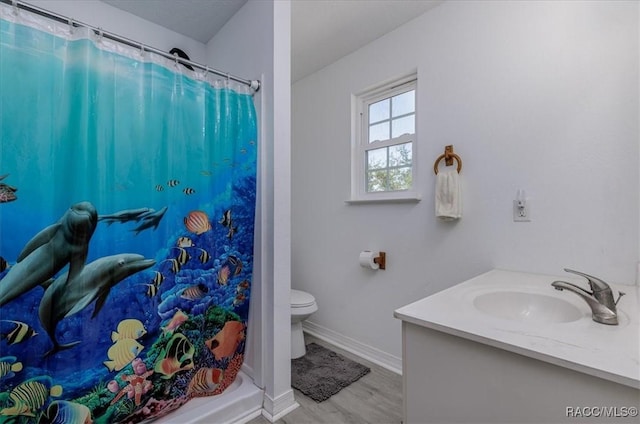bathroom with vanity, wood finished floors, curtained shower, toilet, and baseboards