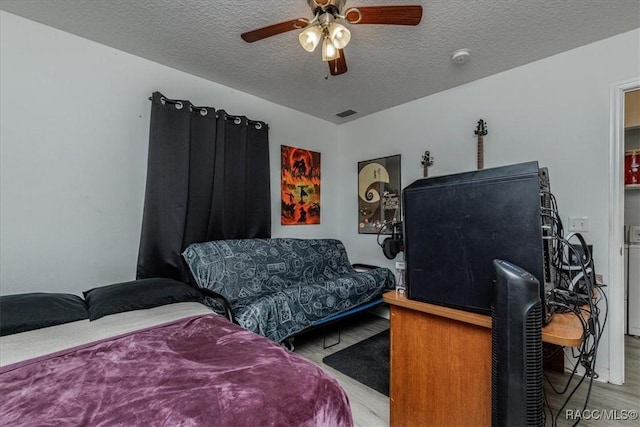 bedroom with ceiling fan, a textured ceiling, visible vents, and wood finished floors