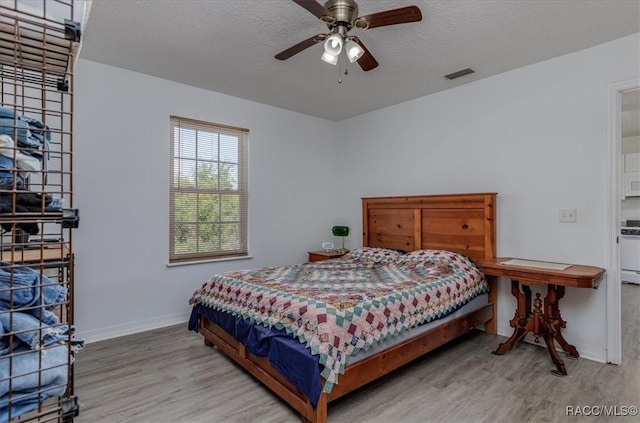 bedroom featuring visible vents, a textured ceiling, baseboards, and wood finished floors