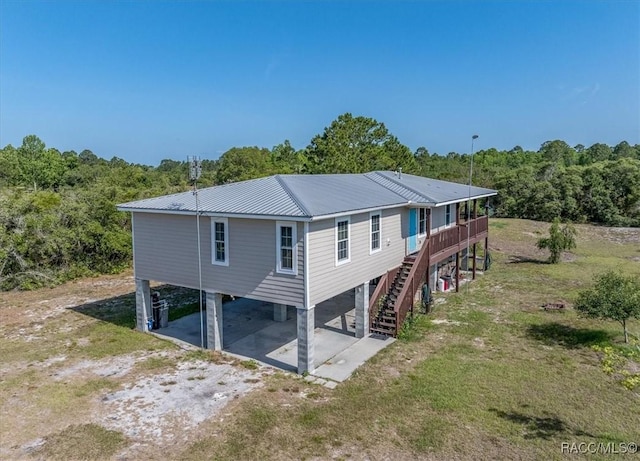 back of property with metal roof, dirt driveway, a wooden deck, a carport, and stairs