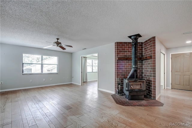 unfurnished living room with a wood stove, a textured ceiling, light hardwood / wood-style flooring, and ceiling fan