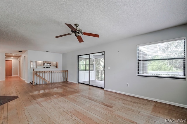 empty room featuring ceiling fan, plenty of natural light, a textured ceiling, and light wood-type flooring