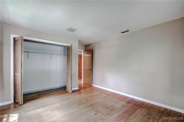 unfurnished bedroom with a textured ceiling, light hardwood / wood-style floors, and a closet