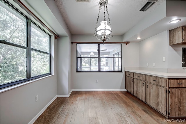 unfurnished dining area featuring a chandelier, light wood-type flooring, and plenty of natural light