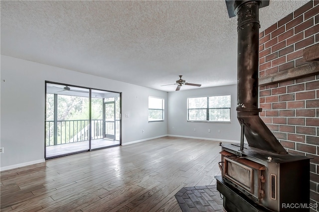 unfurnished living room featuring a healthy amount of sunlight, wood-type flooring, a wood stove, and a textured ceiling