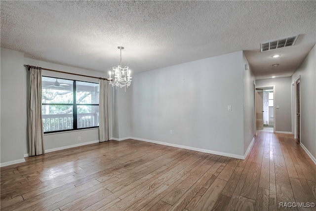 empty room with a textured ceiling, light hardwood / wood-style floors, and an inviting chandelier