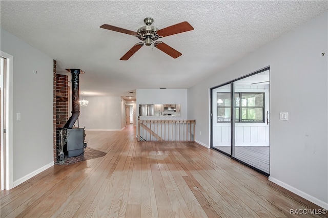 unfurnished living room with a wood stove, ceiling fan, wood-type flooring, and a textured ceiling