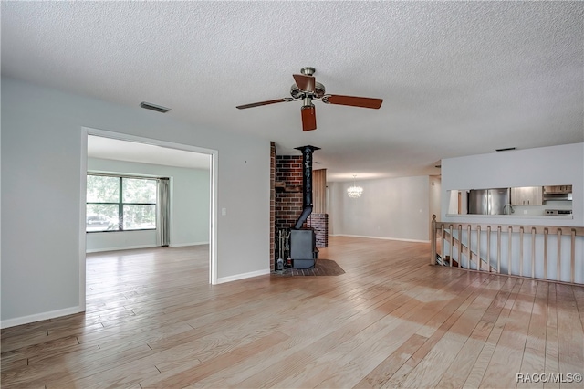 unfurnished living room with a textured ceiling, light hardwood / wood-style flooring, a wood stove, and ceiling fan