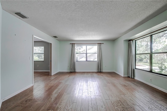 unfurnished room featuring a wealth of natural light, light hardwood / wood-style floors, and a textured ceiling