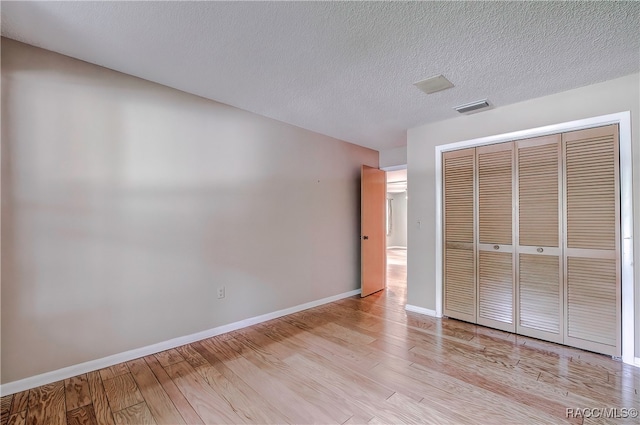 unfurnished bedroom featuring a textured ceiling, light hardwood / wood-style floors, and a closet