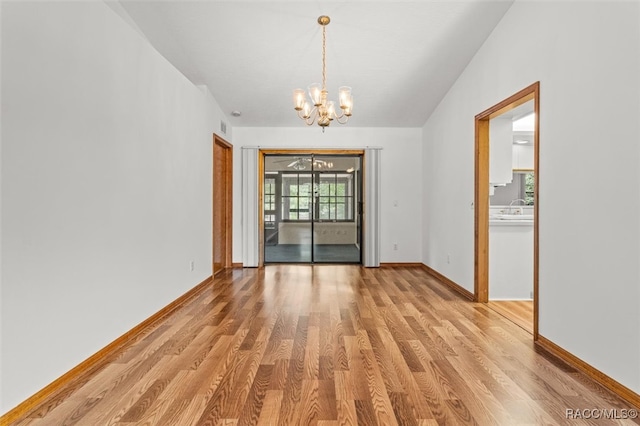 unfurnished dining area with light wood-type flooring, an inviting chandelier, vaulted ceiling, and sink