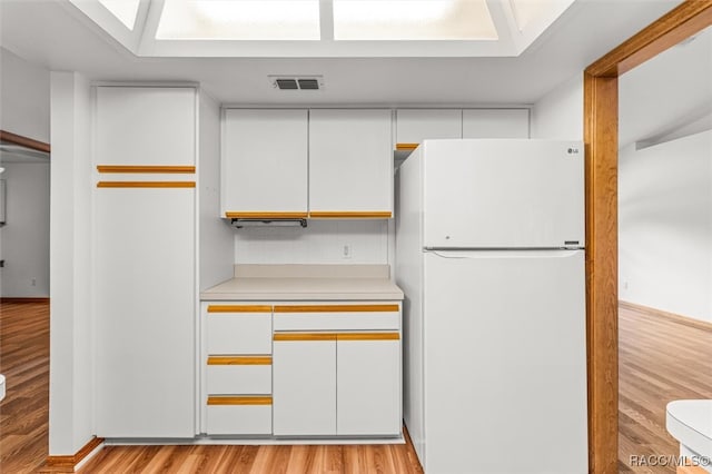 kitchen with white cabinets, light hardwood / wood-style floors, and white refrigerator