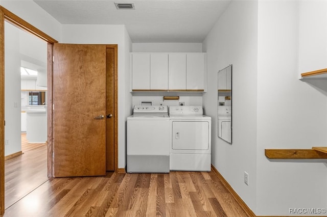 laundry area featuring washer and dryer, cabinets, and light wood-type flooring