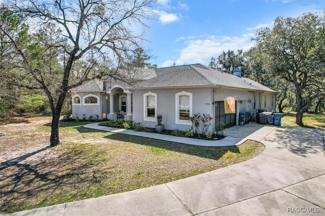 view of front of property with a front yard, concrete driveway, roof with shingles, and stucco siding