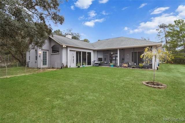 rear view of property featuring a sunroom, a yard, a chimney, and stucco siding