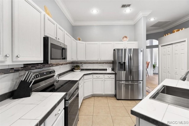 kitchen featuring tile countertops, stainless steel appliances, visible vents, backsplash, and white cabinetry