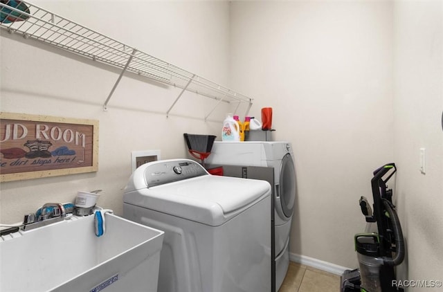 clothes washing area featuring washer and clothes dryer, light tile patterned flooring, a sink, laundry area, and baseboards