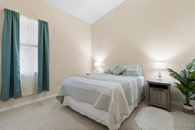 bedroom with baseboards, vaulted ceiling, and light colored carpet