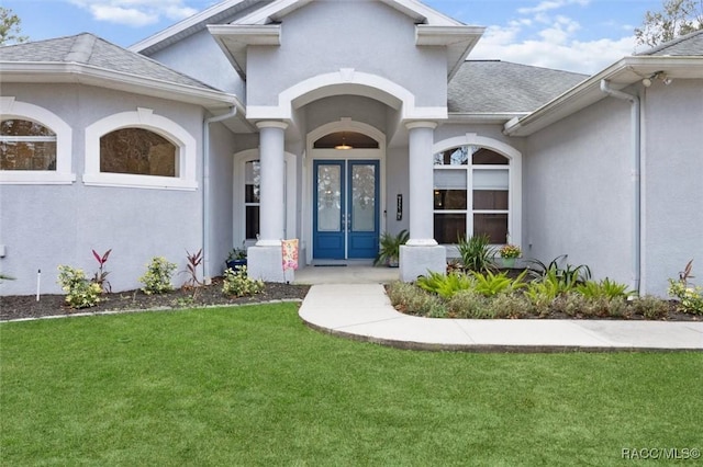 property entrance featuring a shingled roof, french doors, a lawn, and stucco siding