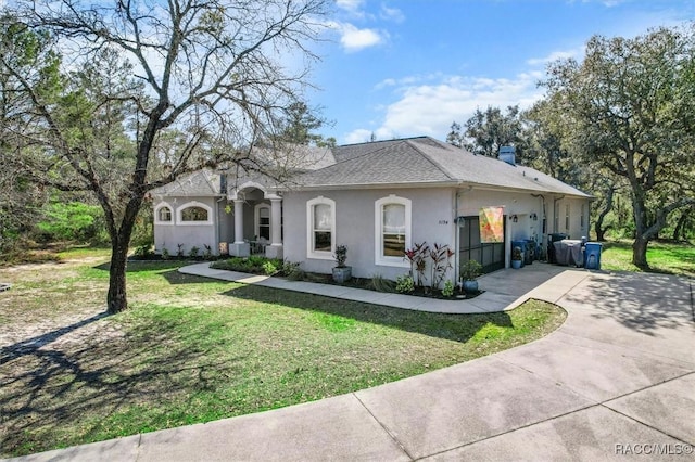 view of front of house featuring driveway, a chimney, roof with shingles, a front lawn, and stucco siding