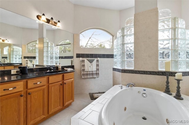 bathroom featuring tile patterned flooring, a tub with jets, tile walls, and vanity