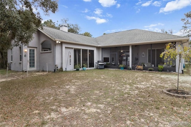 back of property featuring a shingled roof, a sunroom, a chimney, and stucco siding