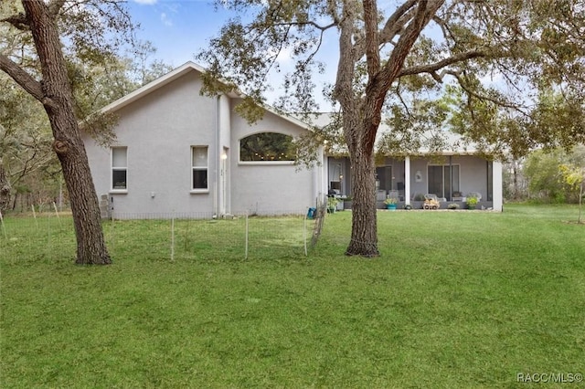 rear view of house featuring a sunroom, stucco siding, and a yard