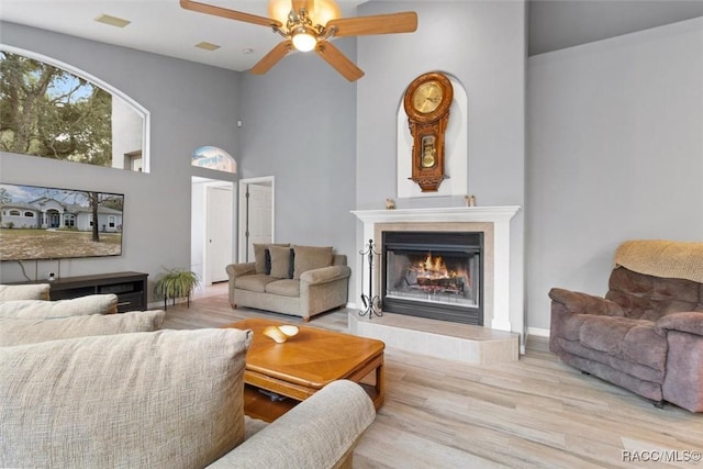 living room with baseboards, a towering ceiling, ceiling fan, light wood-style floors, and a fireplace