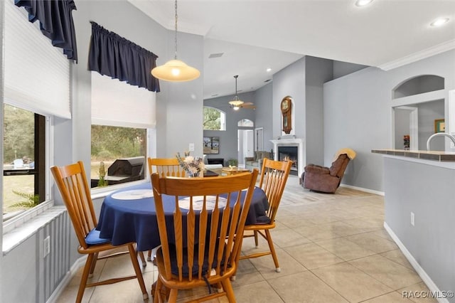 dining space with a warm lit fireplace, baseboards, a high ceiling, crown molding, and light tile patterned flooring