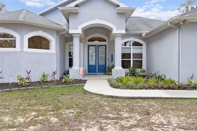 doorway to property featuring a yard, roof with shingles, and stucco siding