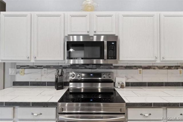 kitchen featuring stainless steel appliances, dark countertops, white cabinets, and decorative backsplash