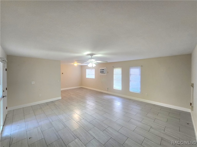 spare room featuring ceiling fan, light wood-type flooring, an AC wall unit, and a textured ceiling