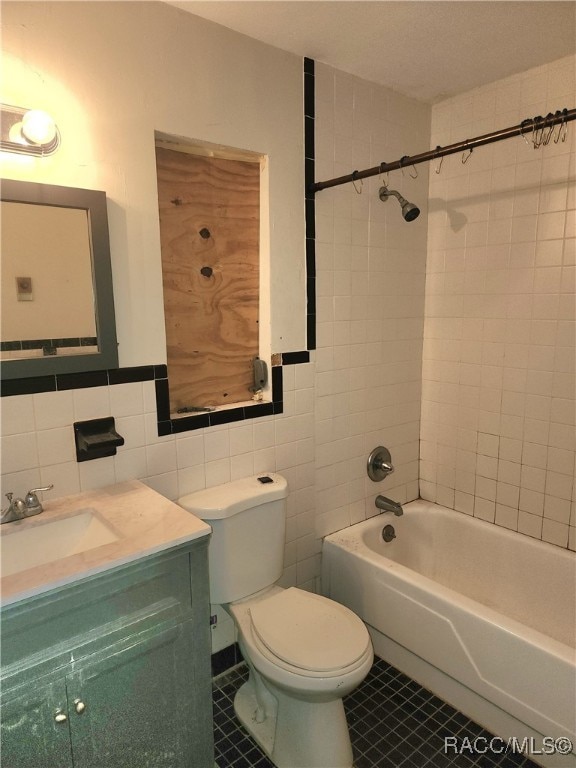 full bathroom featuring tiled shower / bath combo, tile patterned flooring, toilet, vanity, and tile walls