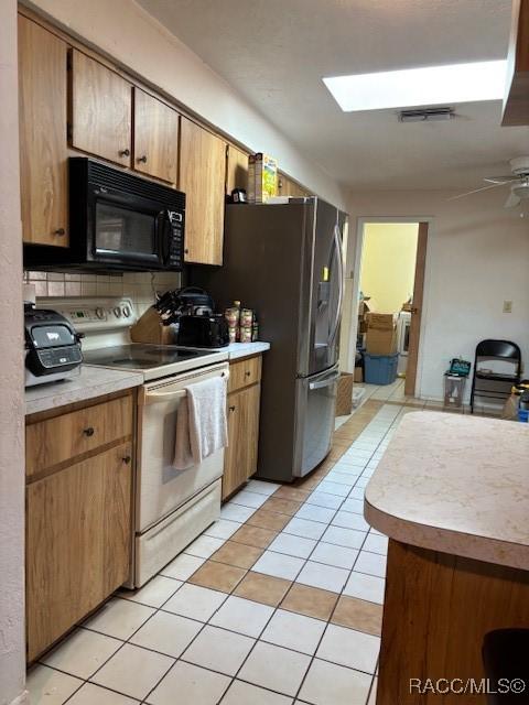 kitchen with electric stove, black microwave, light countertops, and light tile patterned flooring