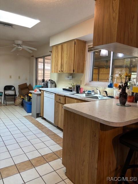 kitchen with brown cabinets, light countertops, white dishwasher, a sink, and a peninsula