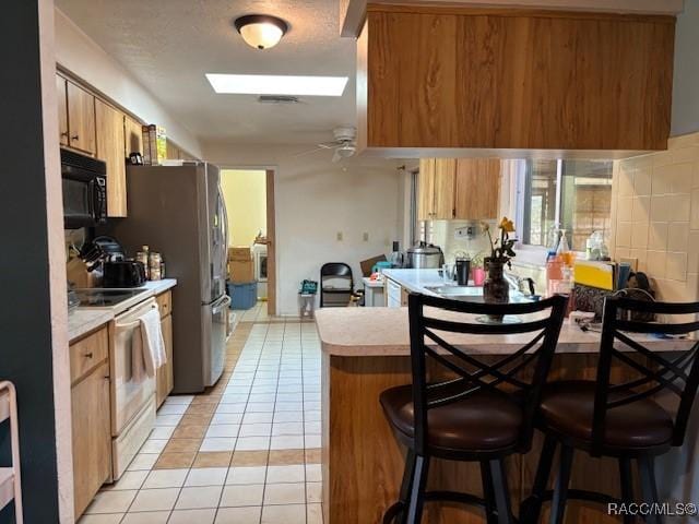 kitchen featuring a breakfast bar, electric range, black microwave, and light countertops