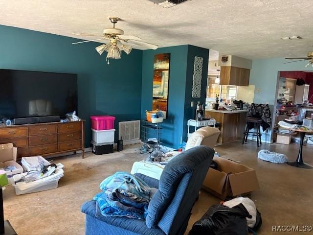 living room featuring ceiling fan, visible vents, and a textured ceiling