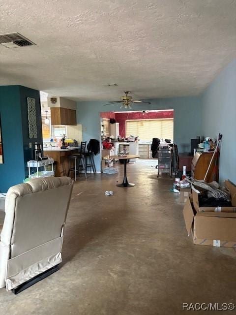 living area with concrete flooring, visible vents, a textured ceiling, and a ceiling fan