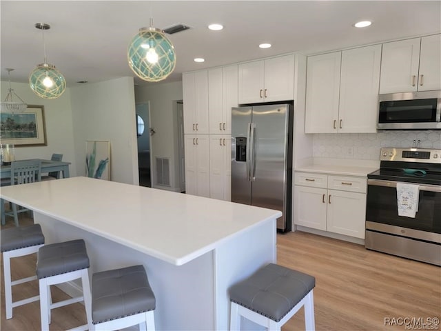 kitchen featuring appliances with stainless steel finishes, decorative light fixtures, white cabinetry, and light hardwood / wood-style flooring