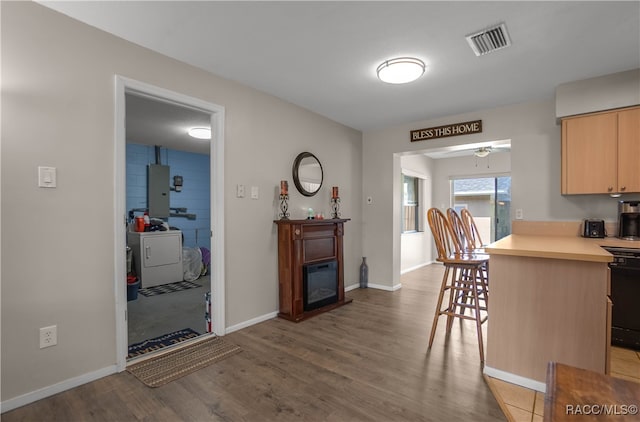 kitchen featuring light brown cabinets, washing machine and dryer, kitchen peninsula, a breakfast bar area, and light wood-type flooring