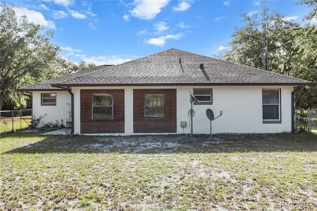 rear view of house featuring fence, a shingled roof, and a yard